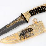 Thin expensive knife with a damascus blade and teeth on the butt. The hilt and scabbard are covered with gold and embossed patterns. The leather handle comfortably lay in the hand and does not slip out when wet.