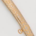 The scabbard of the saber is covered with gold and carved ornament made by the method of engraving on the metal surface.