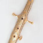 تم تزيين السيف الذهبي بشكل رائع بزخارف زهرية مصنوعة من النقش اليدوي والأحجار المرصعة.