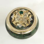 Metal parts of the stone case are made according to the sketch of the designer and plated with nickel and gold. Gold is combined with a rich green shade of natural stone. A large green stone is inlaid in the handle of the casket. The bezel is decorated with a ring of transparent phianites.