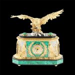 The malachite clock case is equipped with a movement which is presented on the front side with a round dial of small diameter. Roman numerals are depicted on a golden background of the dial, making the exact time easily distinguishable.